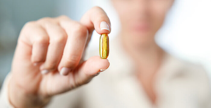 capsule de vitamine D tenue entre les doigts d'une personne en arrière plan