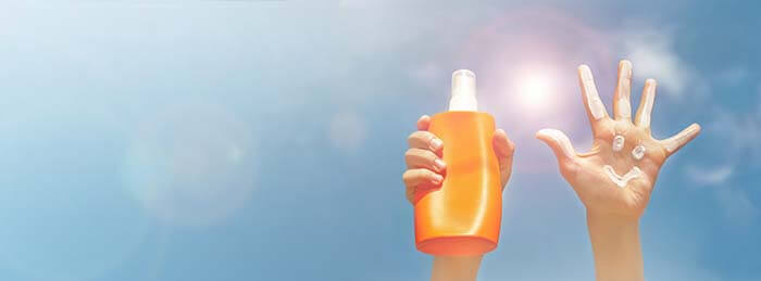 tube de crème solaire et une main enduite de crème brandis sur fond de ciel dégagé