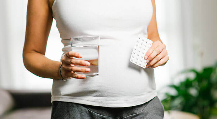 femme enceinte tenant une plaquette d'acide folique d'une main et un verre d'eau de l'autre