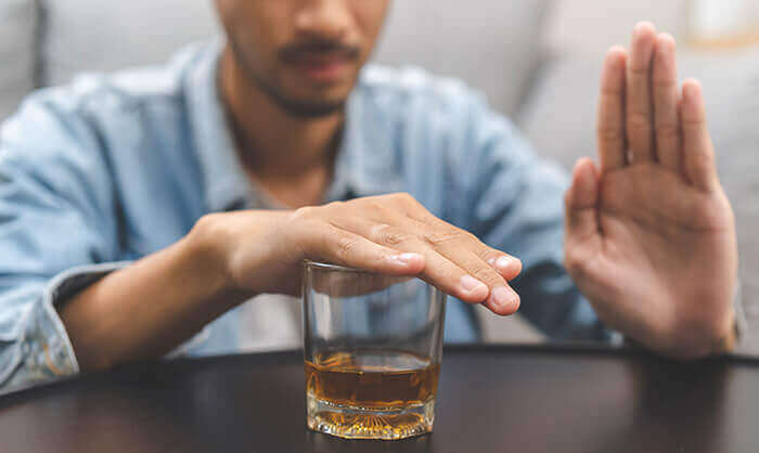 homme faisant le signe stop face à une verre d'alcool