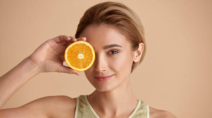 femme à la peau lisse tenant une orange en guise de vitamine C