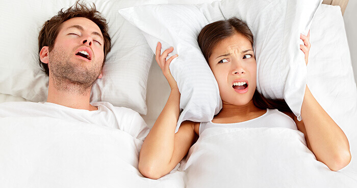 femme dans un lit se bouchant les oreilles à cause des ronflements de son partenaire