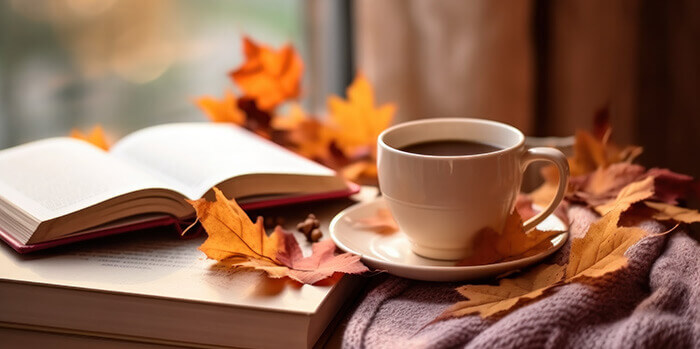 livre posé à côté d'une tasse de café entouré de feuilles d'automne