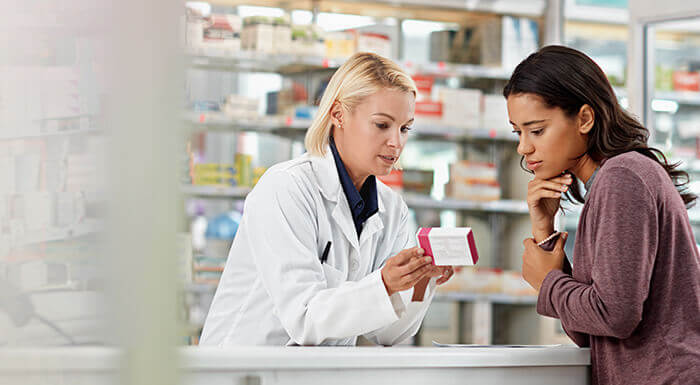 Pharmacienne au comptoir conseillant une patiente sur un médicament