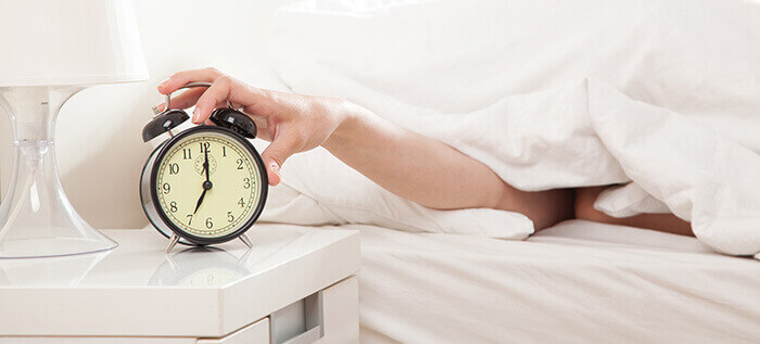 personne éteignant son réveil en tendant le bras de sous une couette