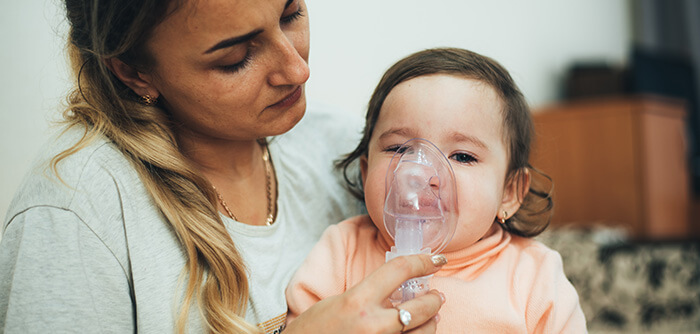 bébé asthmatique sur les genoux de maman avec un masque à oxygène