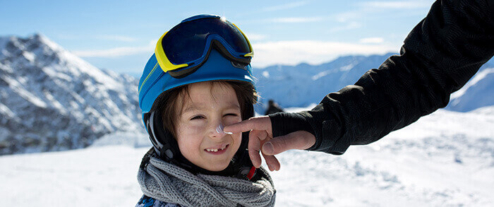 homme appliquant de la crème solaire sur le nez de son enfant au ski