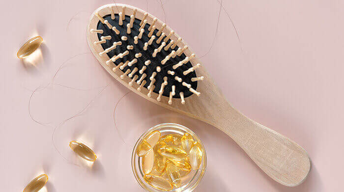 compléments alimentaires accompagnés d'une brosse à cheveux et de quelques cheveux sur fond rose