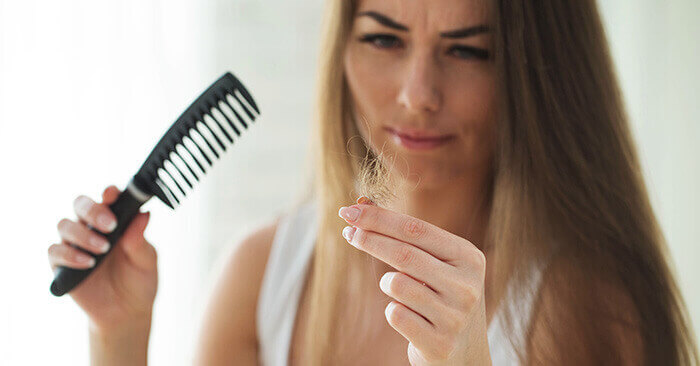 femme à l'air inquiet observant des cheveux qui sont tombés lors du brossage
