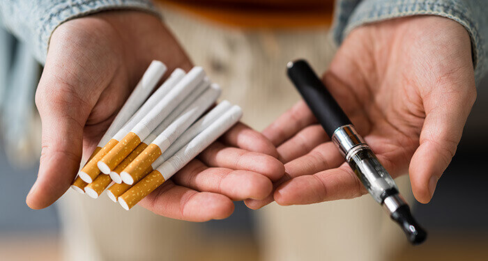 poignée de cigarettes et cigarette électronique présentées dans les mains tendues d'un homme