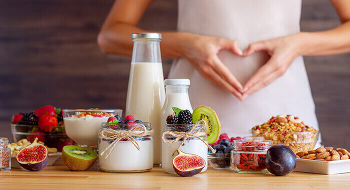 produits laitiers et autres aliments favorisant la digestion posés sur une table avec une femme tenant ses mains en forme de coeur sur son ventre