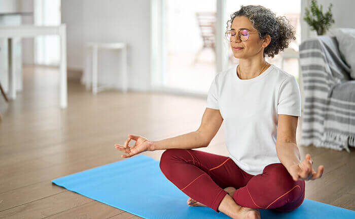 femme méditant sur un tapis de yoga au milieu de son salon