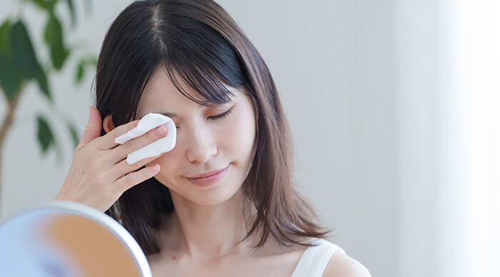 femme se démaquillant délicatement la peau du visage à l'aide d'un coton, face à un miroir