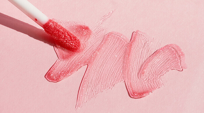 gloss à lèvres rose étalé sur un fond rose à l'aide d'un applicateur