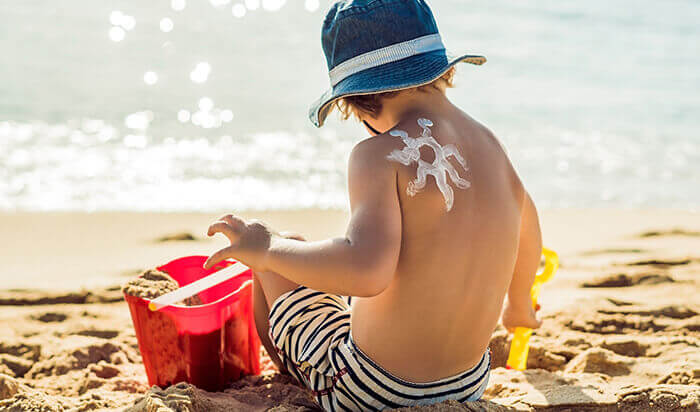 enfant en maillot de bain de dos en train de jouer sur la plage avec un soleil dessiné à la crème solaire sur l'épaule