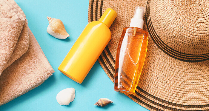 flacons de soins après-soleil sur fond bleu avec des coquillages et un chapeau à larges bords