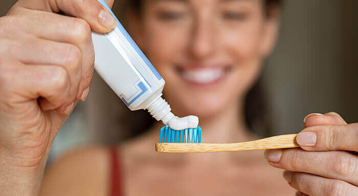 Femme souriante appliquant du dentifrice fluoré sur une brosse à dents