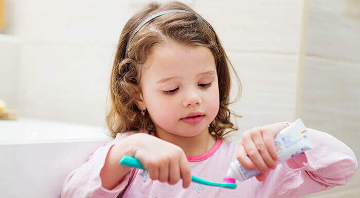 Fillette appliquant du dentifrice sur une brosse à dents