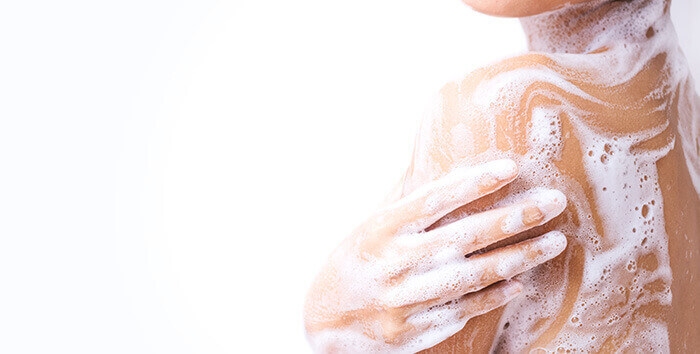 plan sur l'épaule d'une femme faisant mousser du gel douche sur sa peau