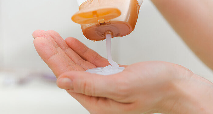 gel douche cremeux coulant d'un flacon dans la paume de main d'une femme
