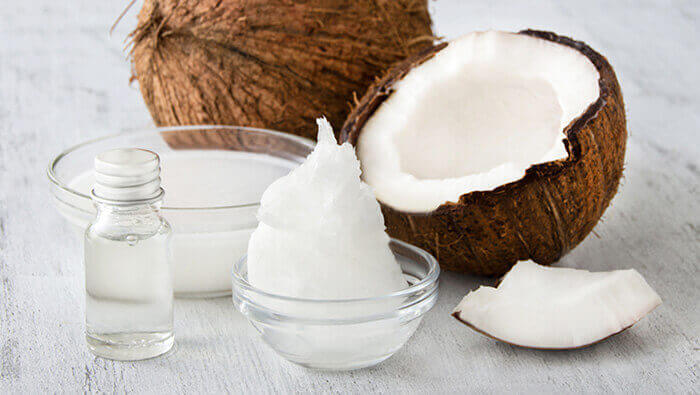 huile de coco solide dans un petit bol à côté d'une fiole d'huile de coco liquide et de noix de coco