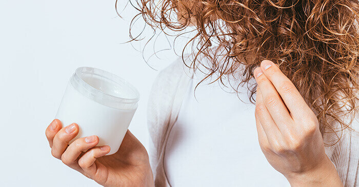 femme hydratant ses cheveux bouclés à l'aide d'une crème hydratante en pot