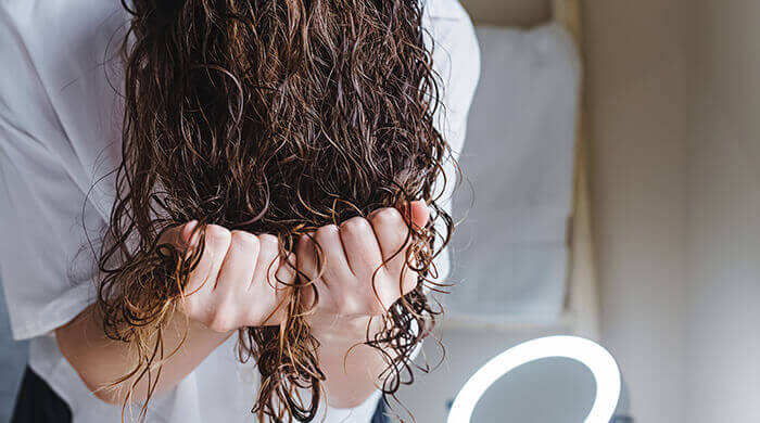 femme réalisant la technique du scrunching sur ses cheveux bouclés