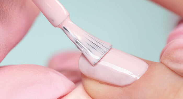 Application de vernis rose clair sur un ongle à l'aide d'un pinceau applicateur