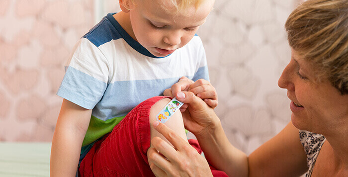 femme appliquant un pansement sur le genou d'un petit garçon