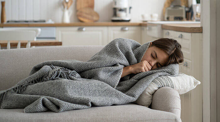 femme atteinte de la grippe se reposant sur un canapé, enroulée dans une couverture