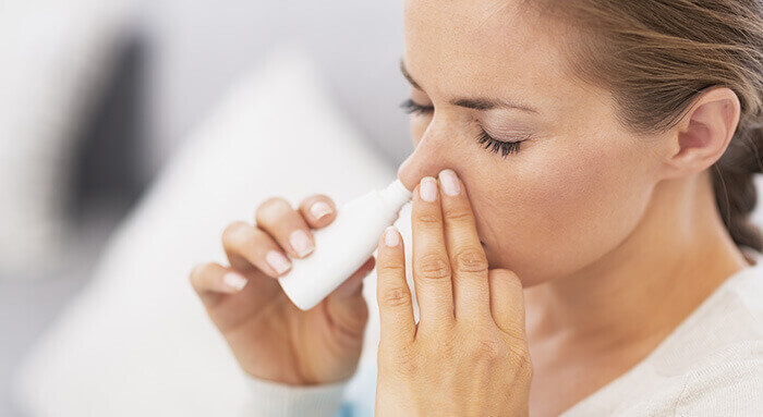 femme réalisant un lavage de nez à l'aide d'un petit flacon blanc