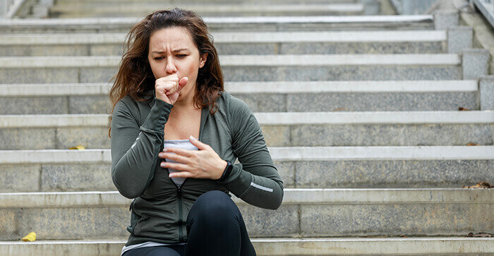 femme assise sur des escaliers, en train de tousser en se tenant la poitrine