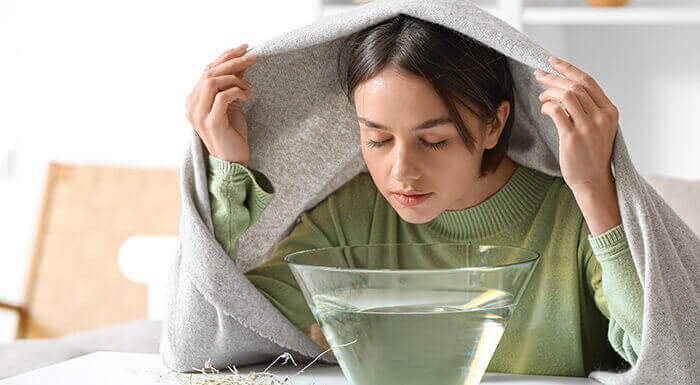 femme pratiquant une inhalation au dessus d'un bol d'eau chaude