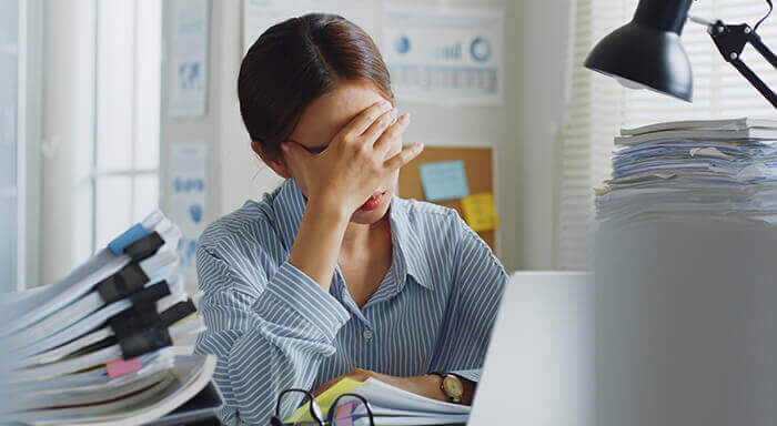 femme se tenant la tête à son bureau débordant de dossier à traiter