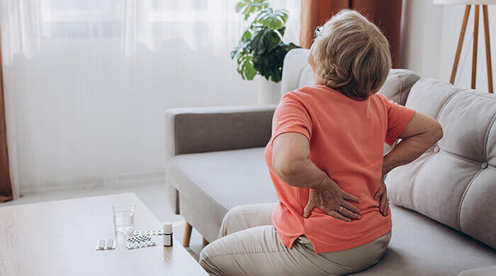 femme se tenant le dos de douleur et flacons de médicaments posés sur une table basse à côté d'elle