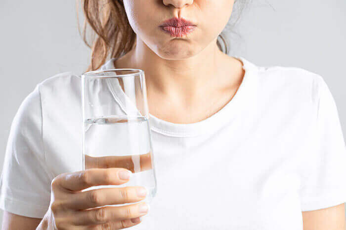 femme effectuant un bain de bouche avec un verre à la main