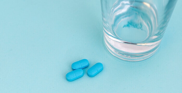 3 comprimés bleus avec un verre d'eau sur un fond bleu