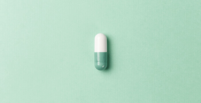 médicament sous forme de gélule verte et blanche sur fond vert