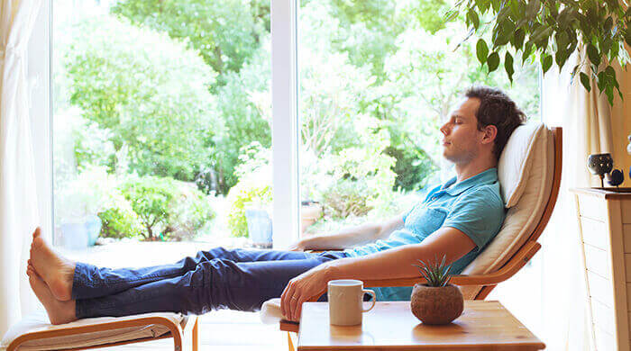 homme se relaxant sur un fauteuil devant une baie vitrée donnant sur un jardin