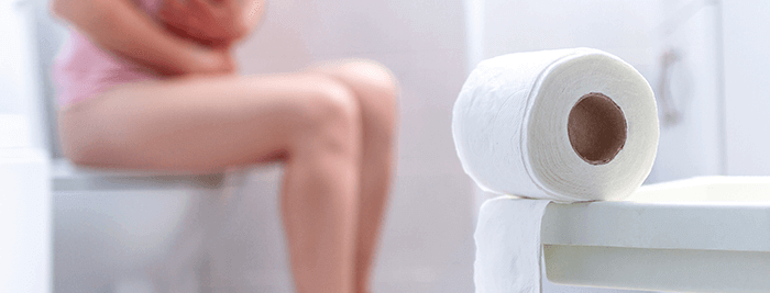 femme assise sur les toilettes souffrant de constipation avec un rouleau de papier toilette en 1er plan
