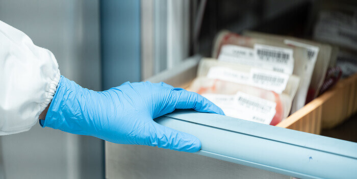 main gantée ouvrant un tiroir frigorifique contenant des pochettes de sang