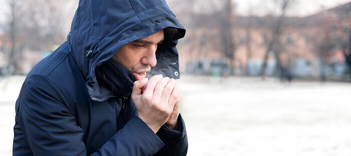homme en veste à capuche soufflant dans ses mains pour les réchauffer