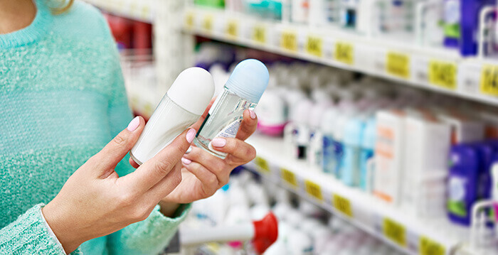 femme comparant 2 déodorants dans une allée de supermarché
