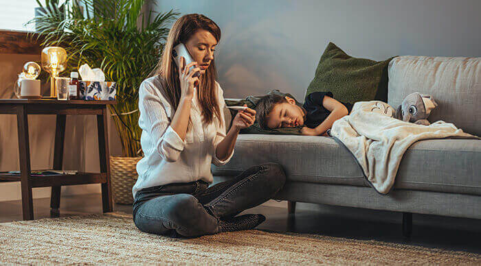 mère au chevet de son garçon fievreux, appelant le médecin tout en consultant le thermomètre