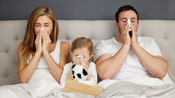 papa, maman et une fillette côte à côte dans un lit, tous les trois en train de se moucher