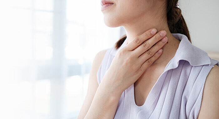 femme se tenant le cou au niveau de la thyroïde