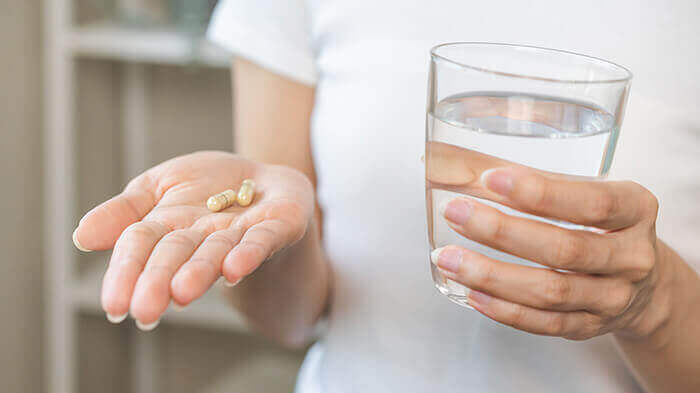 plan sur la main d'une femme tenant deux gélules et un verre d'eau de l'autre