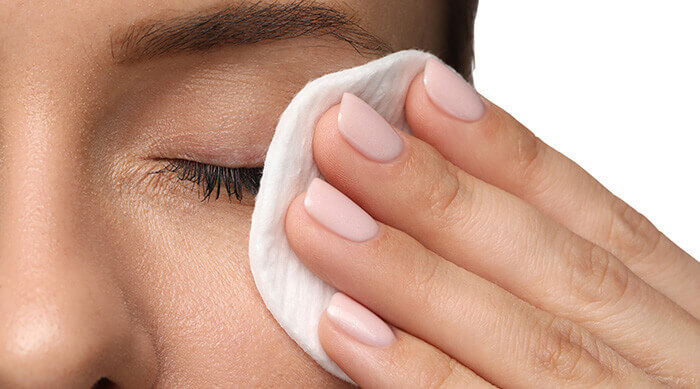 Femme se nettoyant délicatement l'oeil à l'aide d'un coton