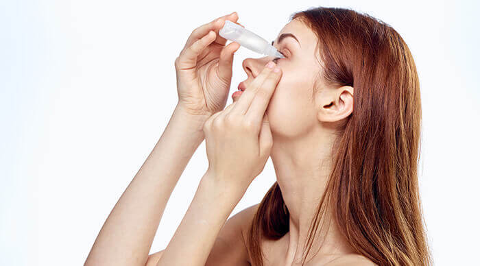 Femme pratiquant un lavage oculaire à l'aide d'une pipette de sérum physiologique