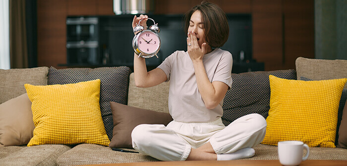 femme fatiguée, en train de bailler en tenant un réveil indiquant 14h